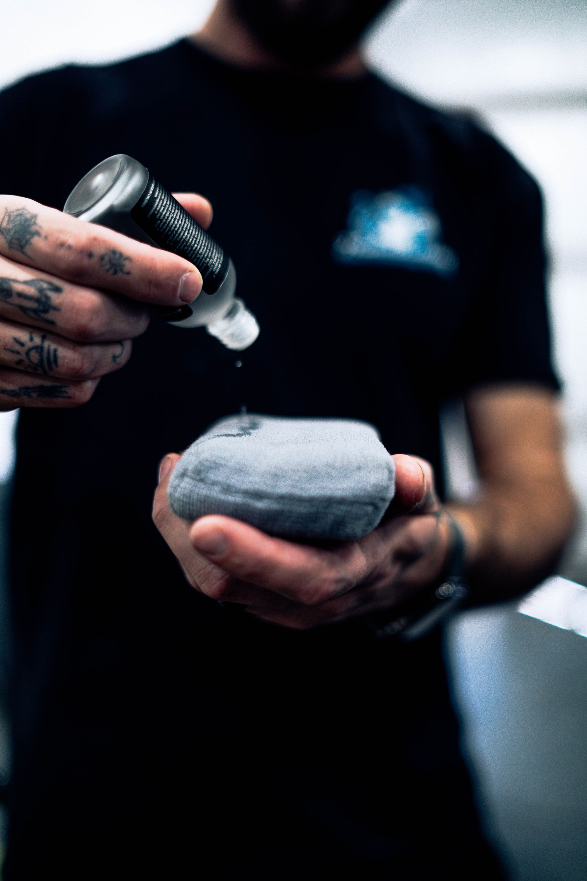 Tattooed hands applying cream to a gray stone against a blurred dark background