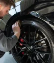 Person polishing a black car wheel with a cloth in a garage