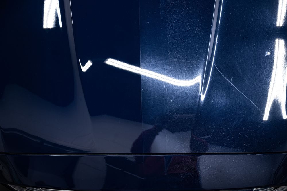 Close-up of a glossy dark blue car hood reflecting bright overhead lights.