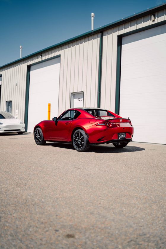 Red sports car parked beside industrial warehouse doors on a sunny day