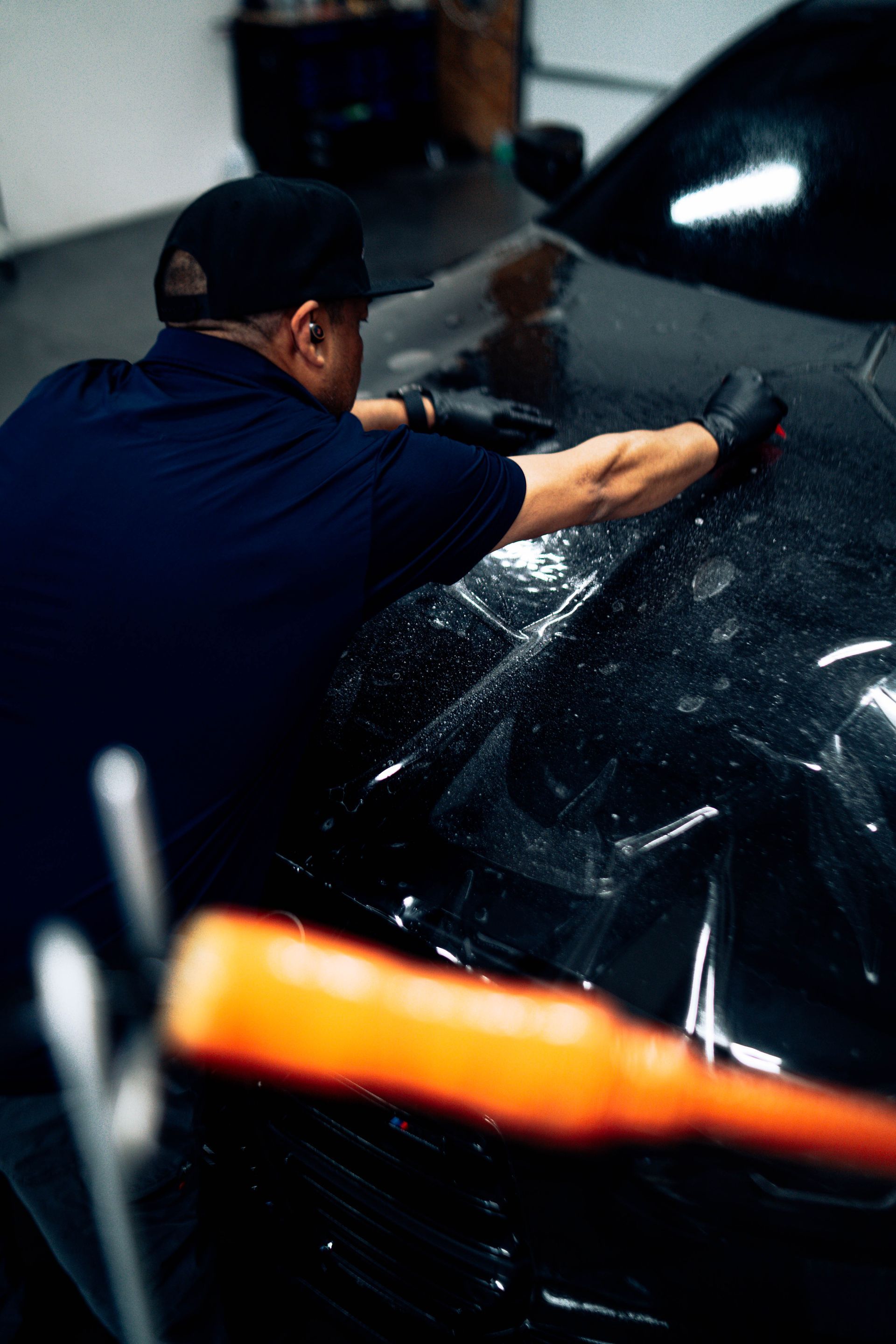 Person polishing a black car hood with a cloth in a garage