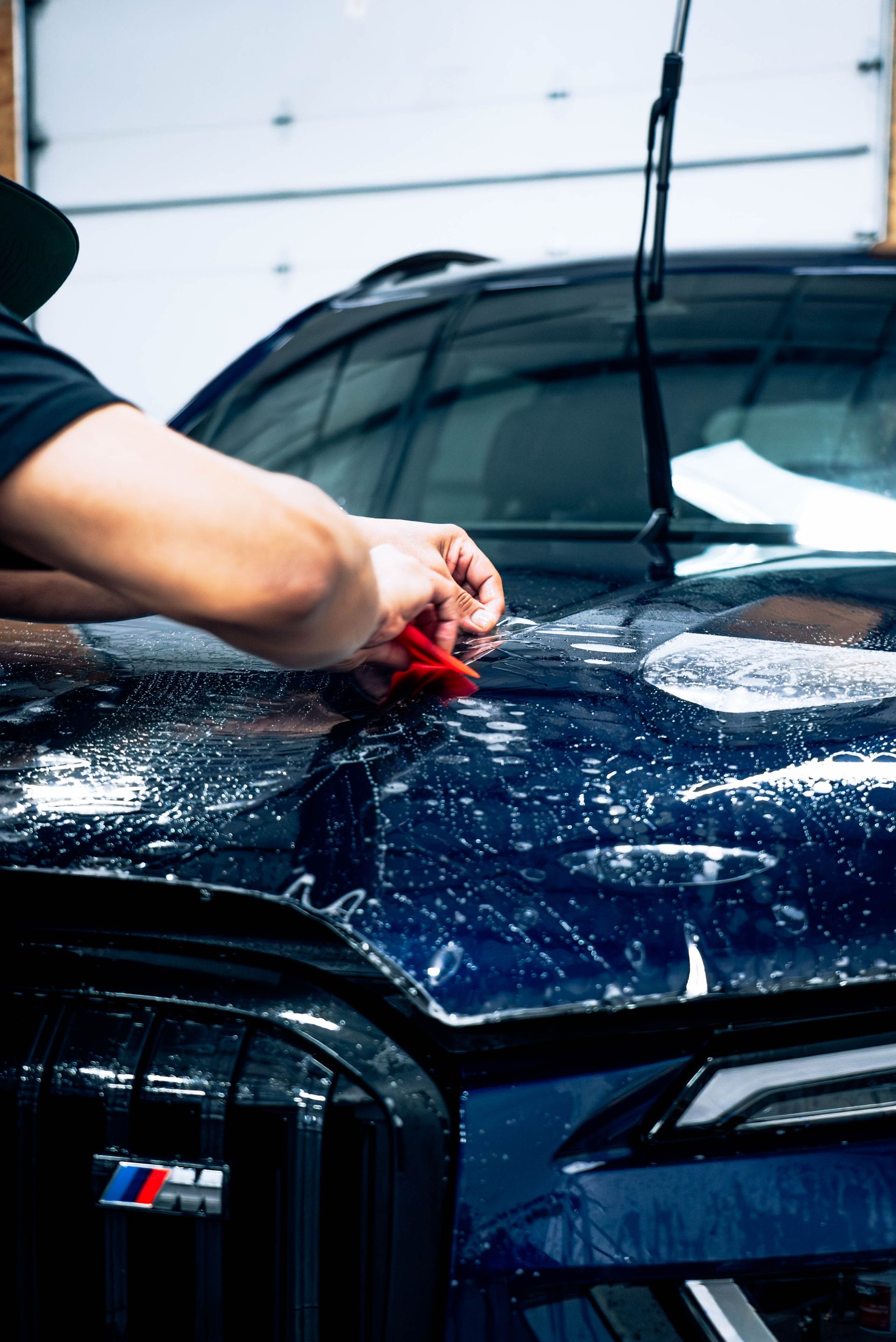 Hand waxing a dark blue BMW hood in a car wash bay