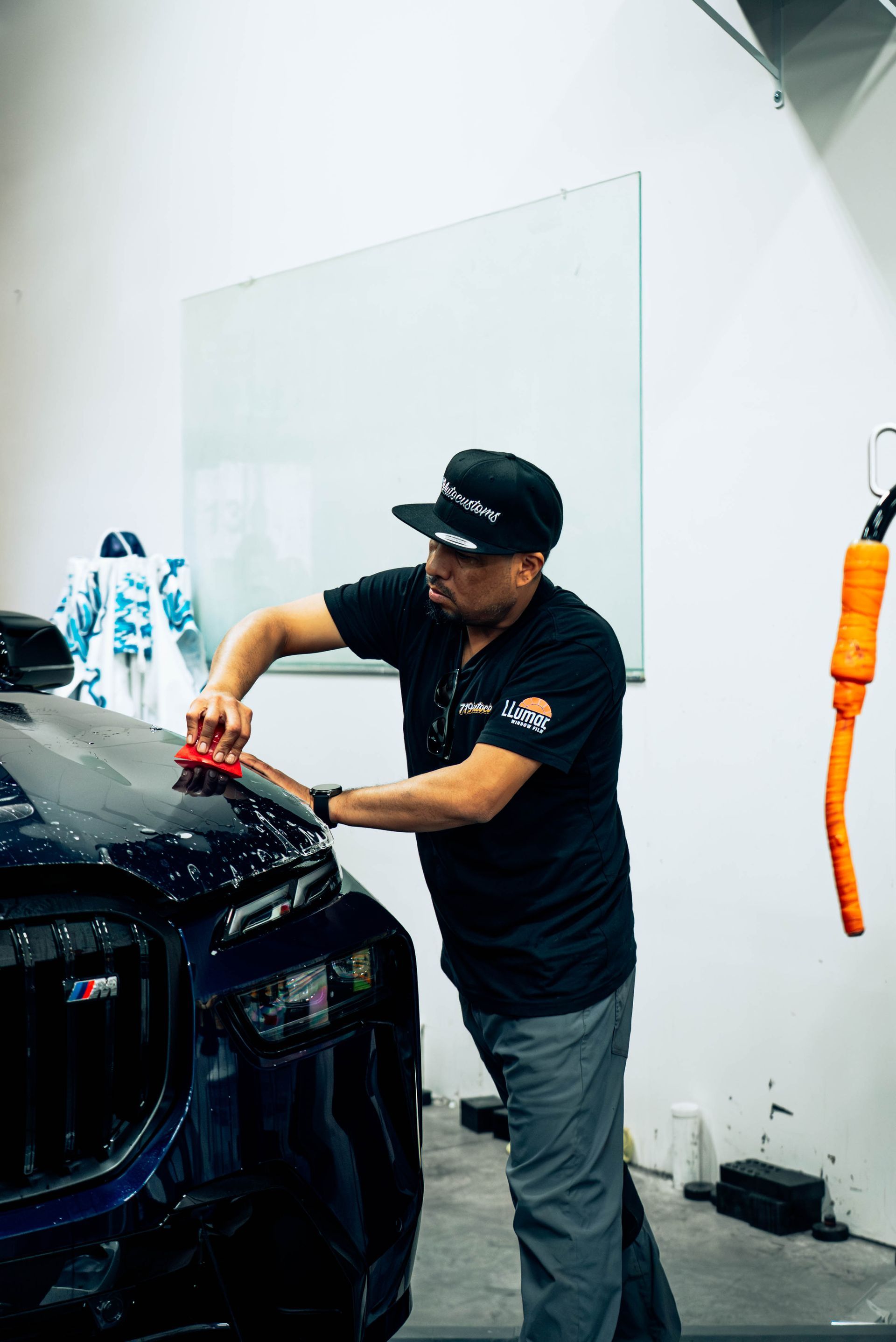 Person polishing a black car in a workshop, using a red cloth.