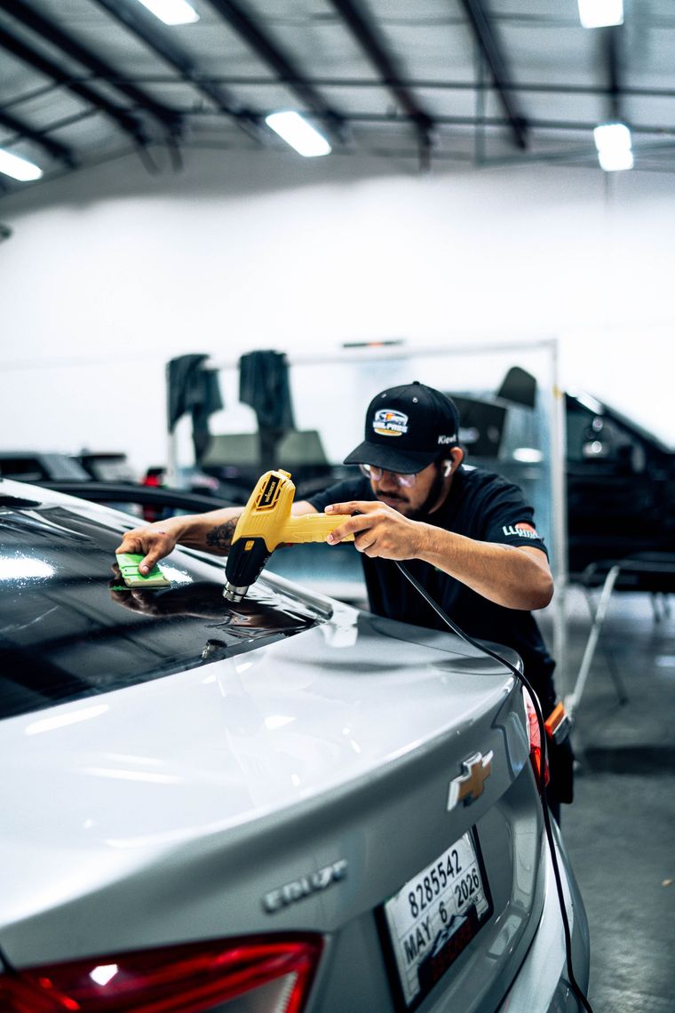 Mechanic polishing a silver car in a garage with a yellow buffer tool