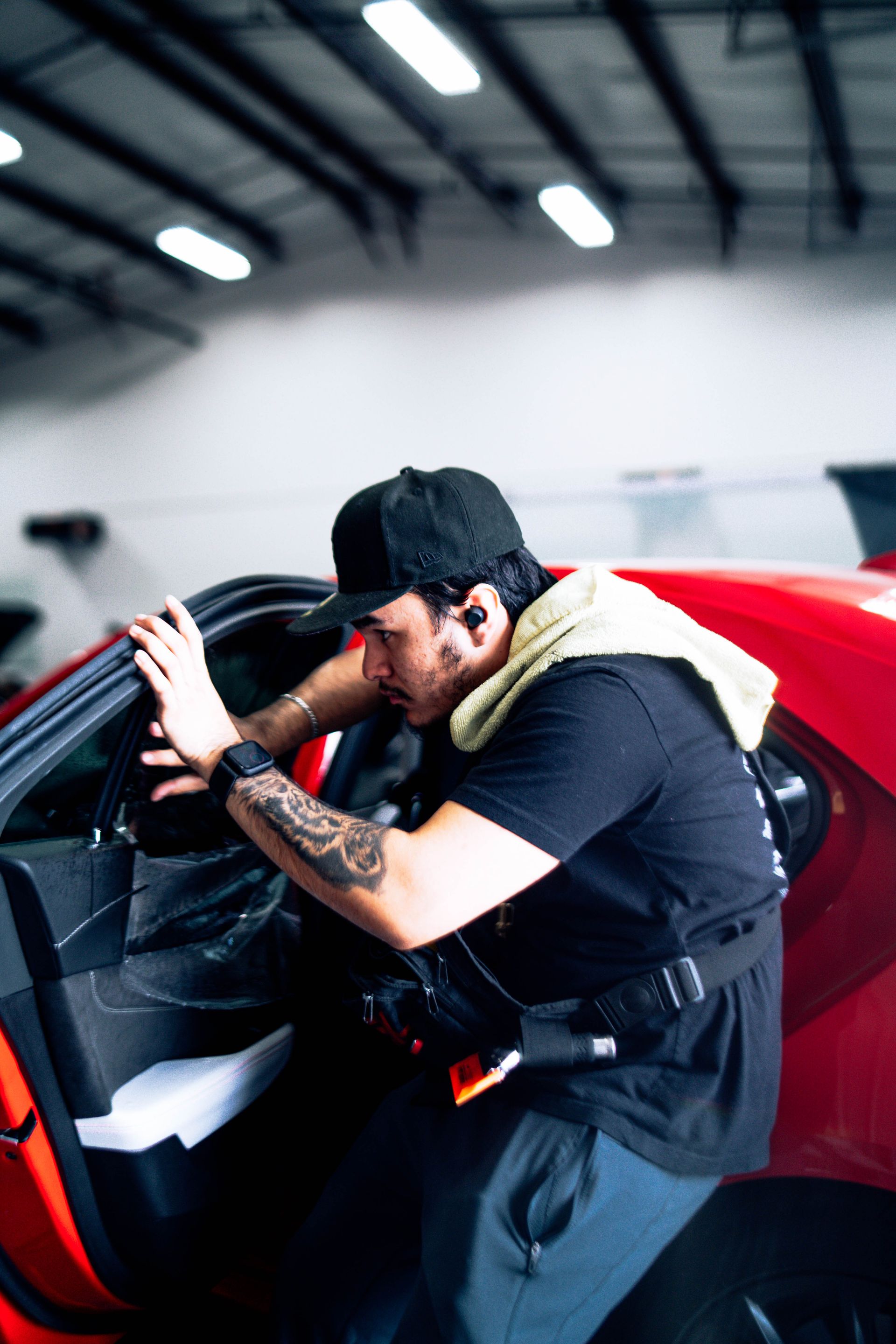 Mechanic inspecting a red car engine in a garage, leaning over the open hood.