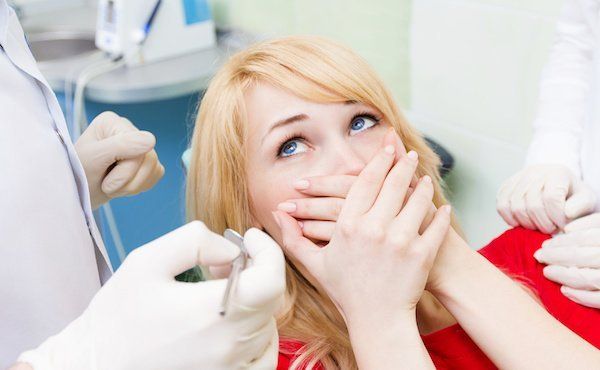 Frau hält sich die Hände vor den Mund beim Zahnarzt, weil sie Angst hat, sie ist Angstpatientin