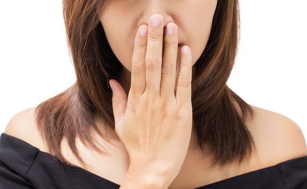 Frau mit Mundgeruch hält sich die Hand vor den Mund