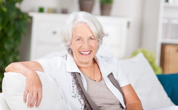 Seniorin sitzt auf dem Sofa mit schönen Zähnen