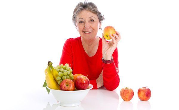 Seniorin sitzt vor Obstkorb und hält einen Apfel in der Hand