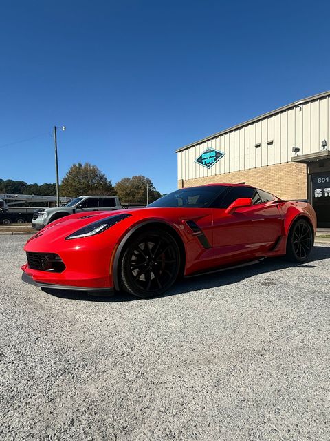 A bright red Chevrolet Corvette parked on a gravel lot under a clear blue sky.