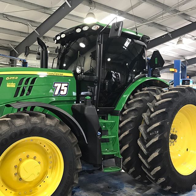 A large, green John Deere tractor with dual rear wheels parked inside a brightly lit industrial maintenance garage.