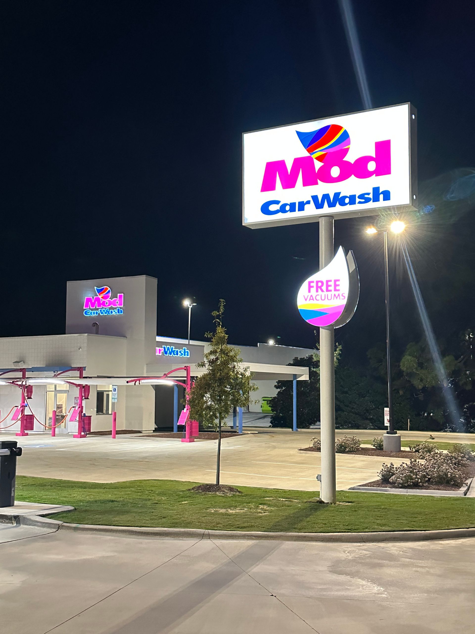An illuminated Mod Car Wash sign and building exterior at night, featuring bright pink lettering and a colorful logo.