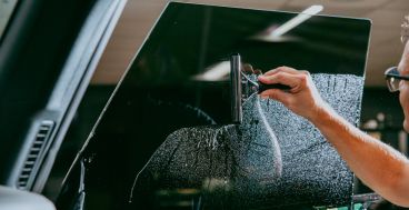 A person uses a squeegee to smooth window tint film onto the inside of a vehicle’s windshield.