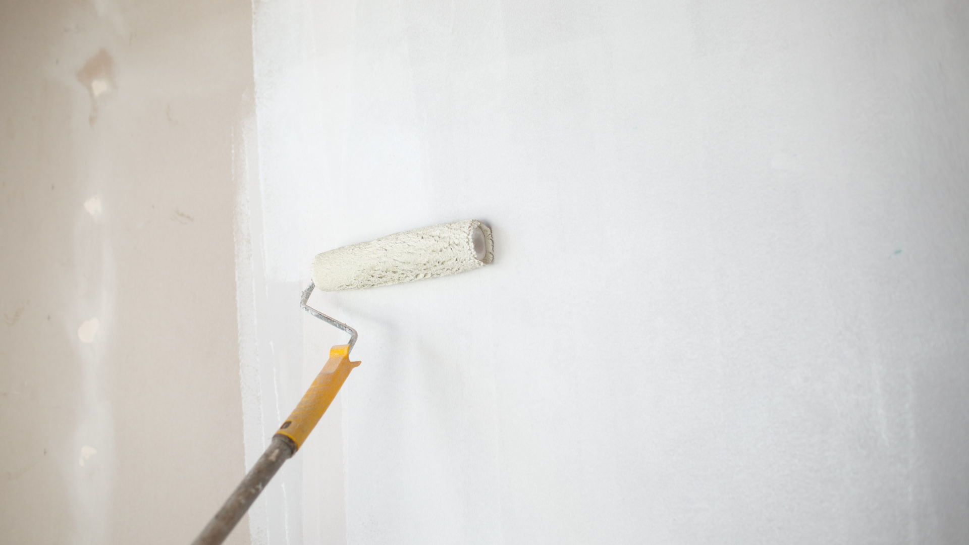A paint roller with white paint applied to a light-colored wall.