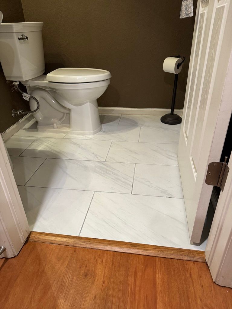 A toilet is sitting on a tiled floor in a bathroom next to a door.
