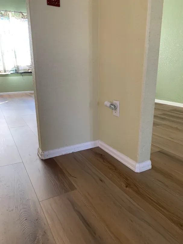 A corner of a room with hardwood floors and a window.