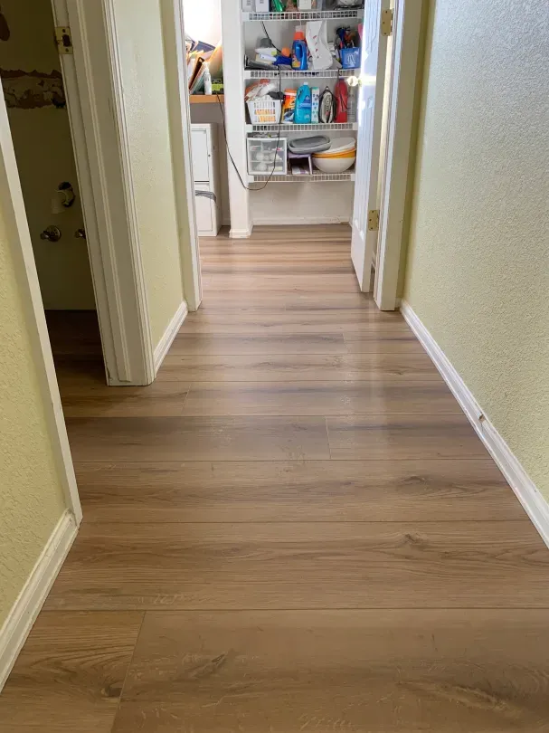 A hallway with hardwood floors and a pantry in the background.