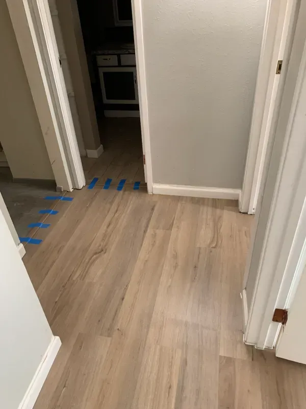 A hallway with hardwood floors and blue tape on the floor.