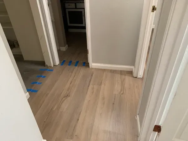 A hallway with a wooden floor and blue tape on the floor.