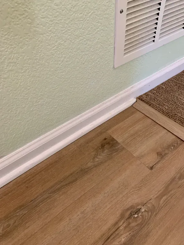 A close up of a wooden floor next to a wall with a vent.