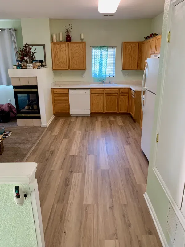 A kitchen with hardwood floors , wooden cabinets , a refrigerator , and a fireplace.