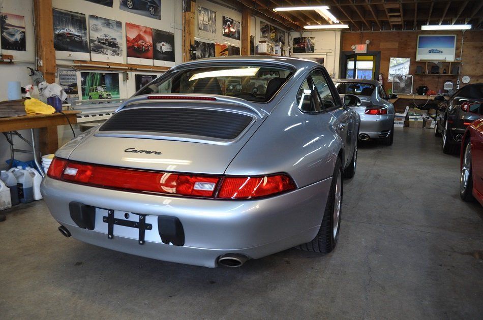 A silver porsche is parked in a garage with other cars