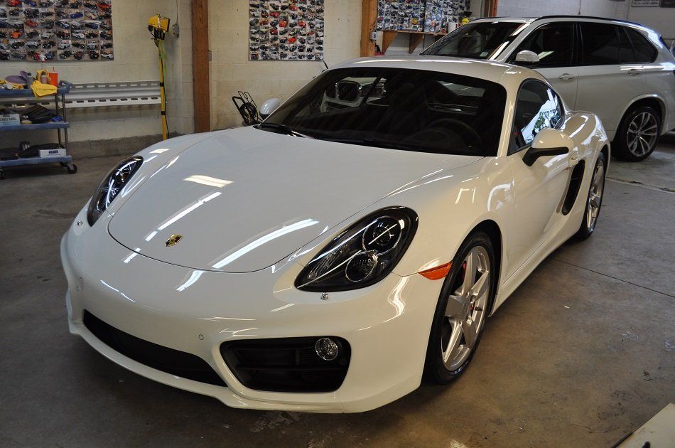 A white porsche boxster is parked in a garage next to a bmw x5.