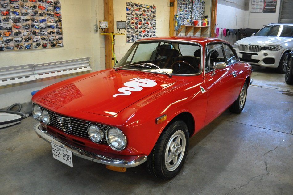A red car is parked in a garage next to a white car.