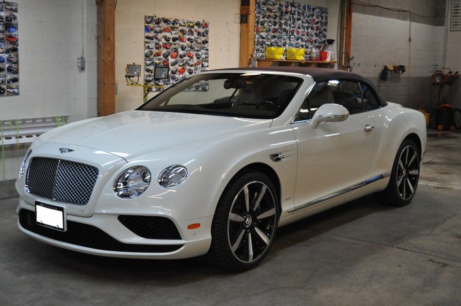 A white bentley convertible is parked in a garage.