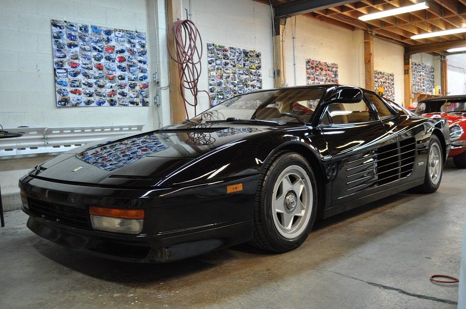A black ferrari testarossa is parked in a garage