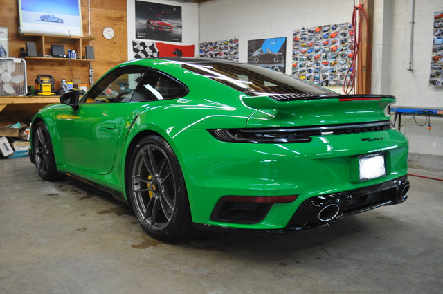A green porsche 911 turbo s is parked in a garage.