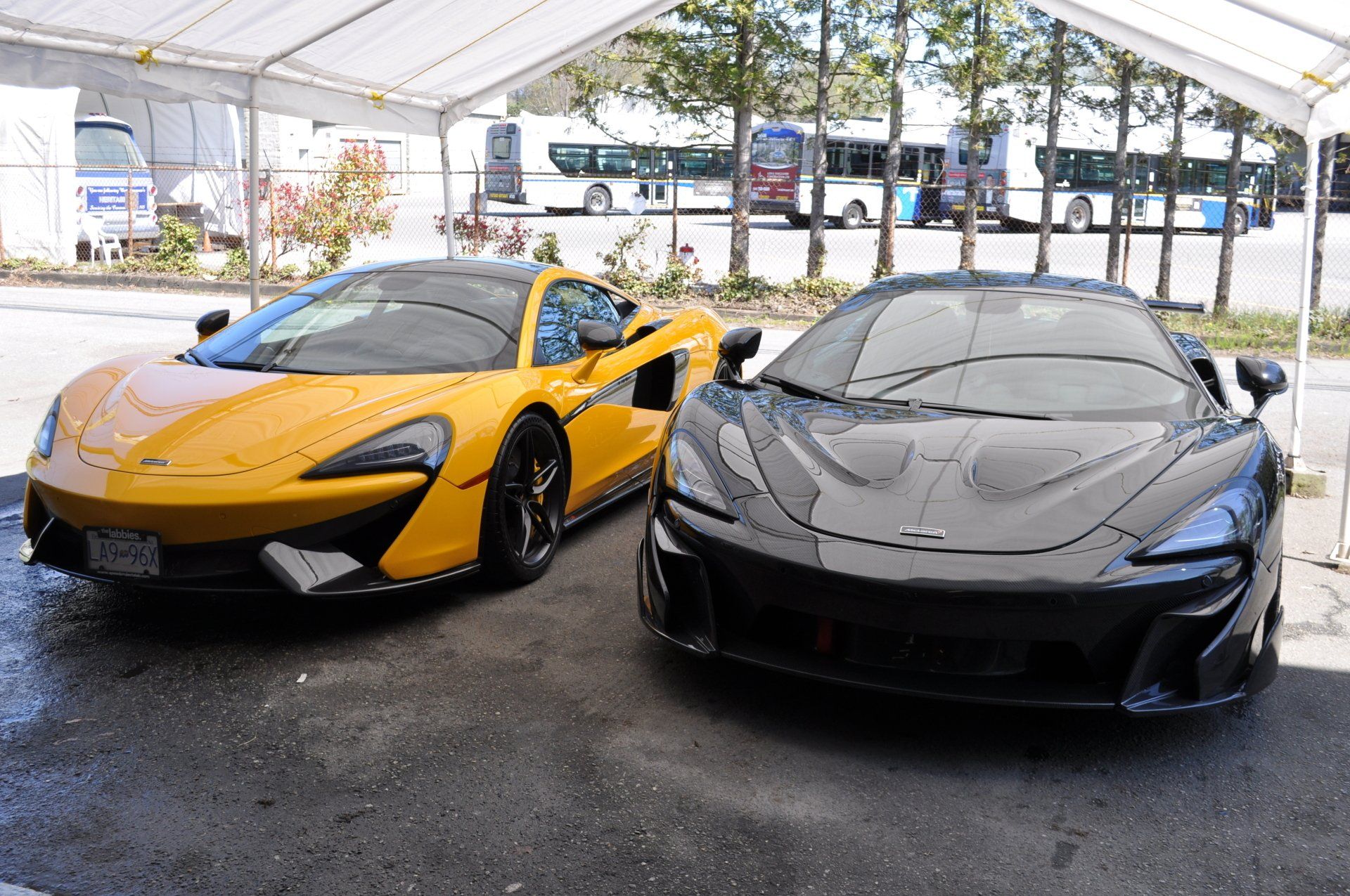 Two sports cars are parked under a tent in a parking lot.
