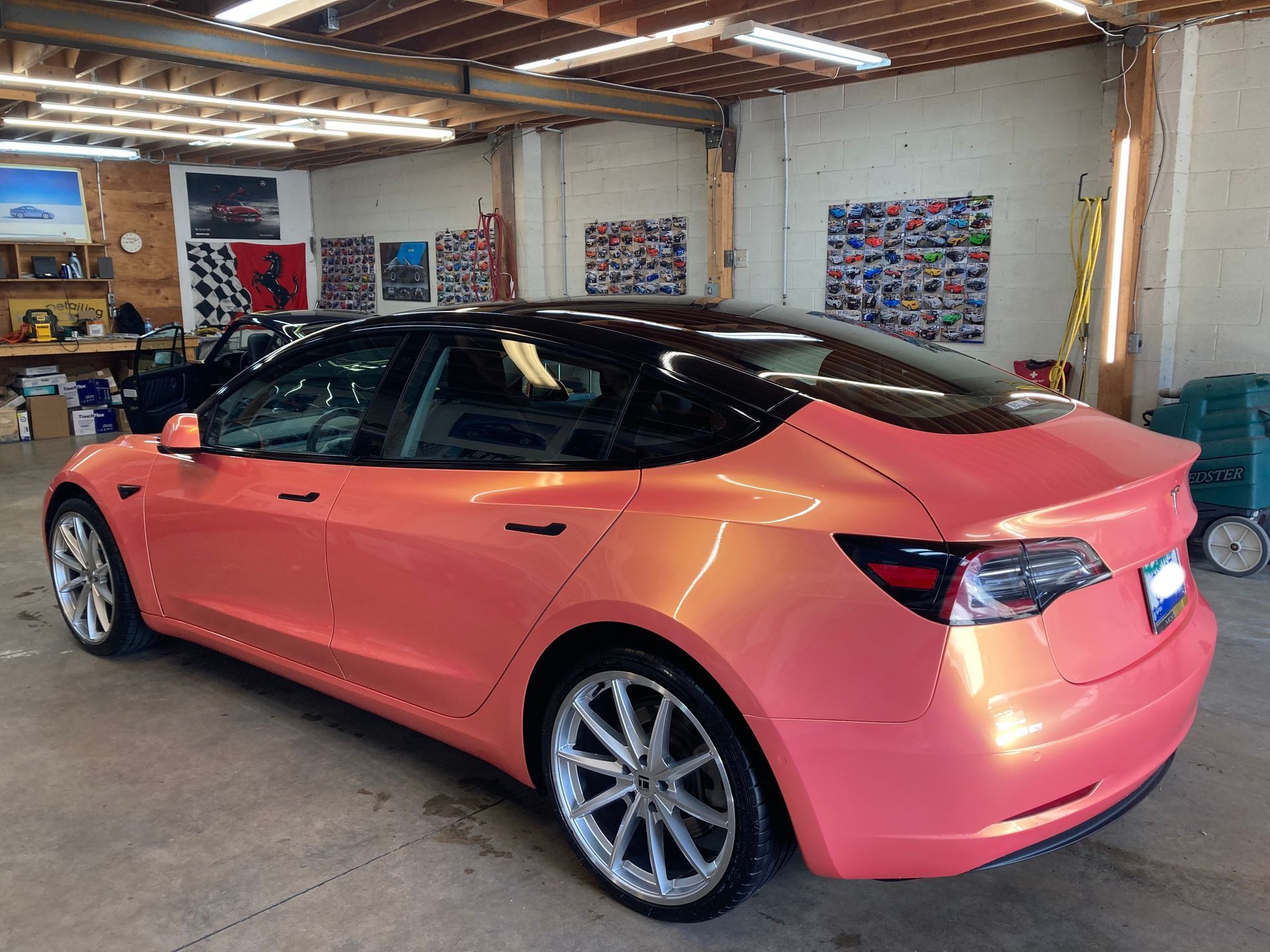 A pink tesla model 3 is parked in a garage