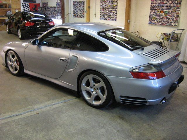 A silver sports car is parked in a garage next to a black car