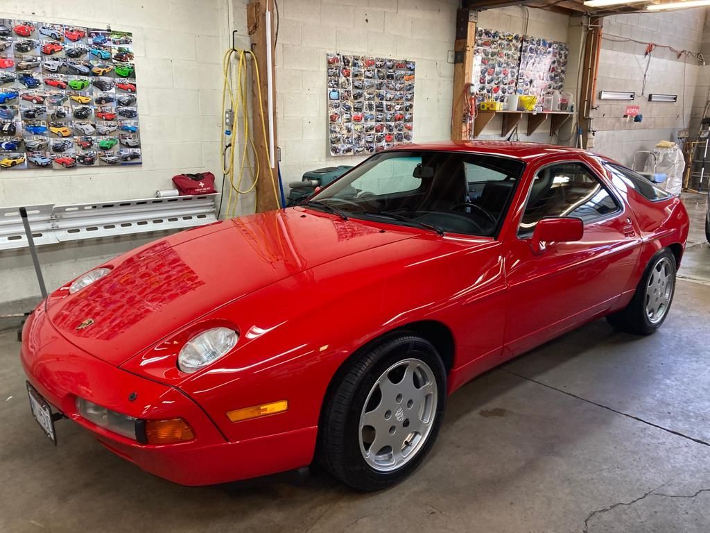 A red porsche 928 is parked in a garage.
