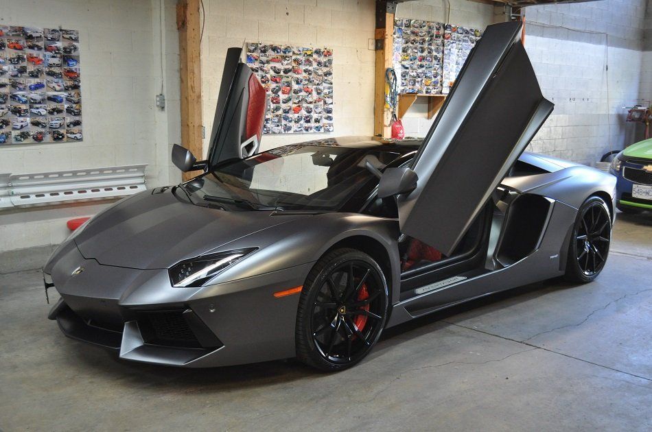 A gray lamborghini aventador is parked in a garage with its doors open.