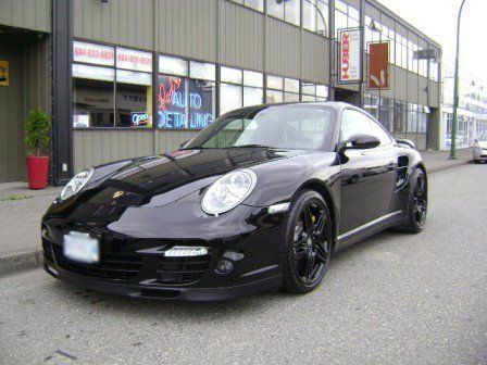 A black sports car is parked in front of a building that says auto detailing