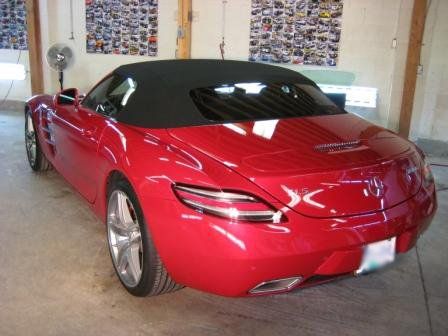 A red sports car with a black top is parked in a garage