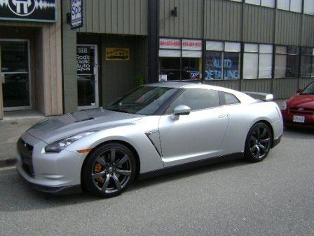 A silver sports car is parked in front of a building that says auto detailing