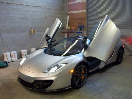 A silver sports car is parked in a garage with its doors open