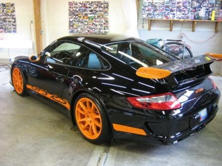 A black porsche with orange wheels is parked in a garage