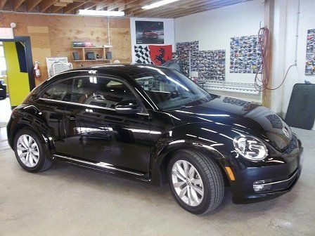 A black volkswagen beetle is parked in a garage