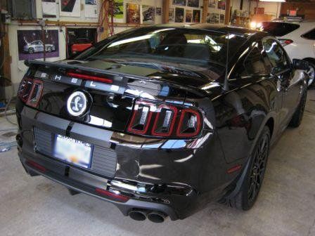 A black mustang is parked in a garage with the trunk open