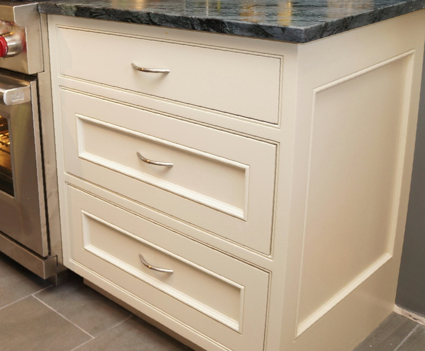 A white cabinet with three drawers and a stove in the background