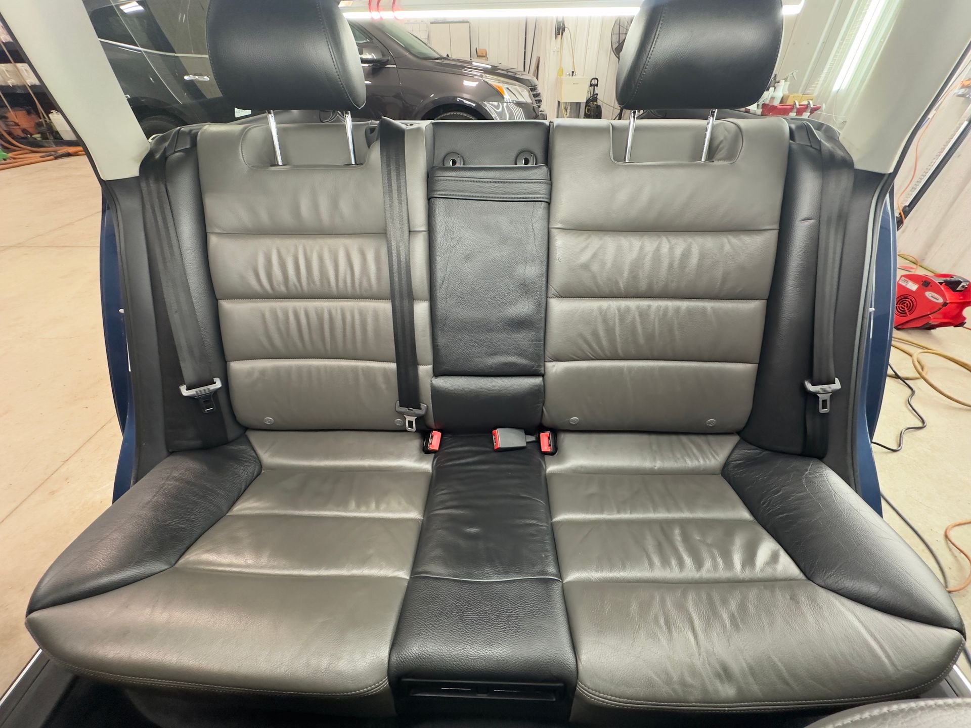 The rear bench seat of a car with grey and black leather upholstery and two adjustable headrests.