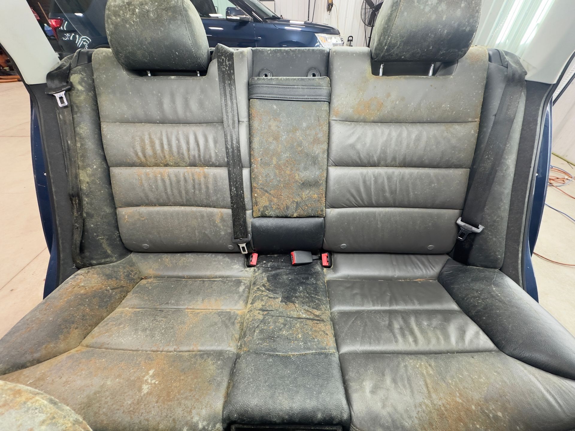 Dirty, dark gray leather back seats of a car covered in light brown debris and dust.