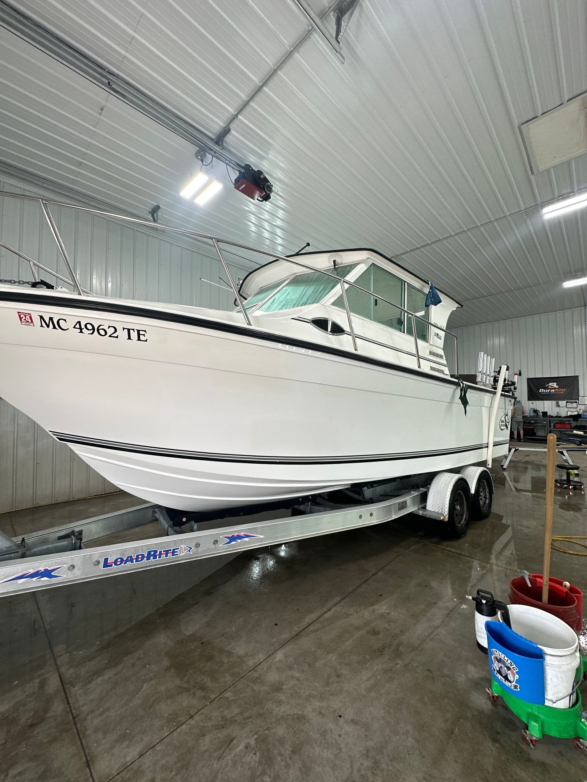 A white motorboat on a metal trailer inside a bright, high-ceiling storage facility.