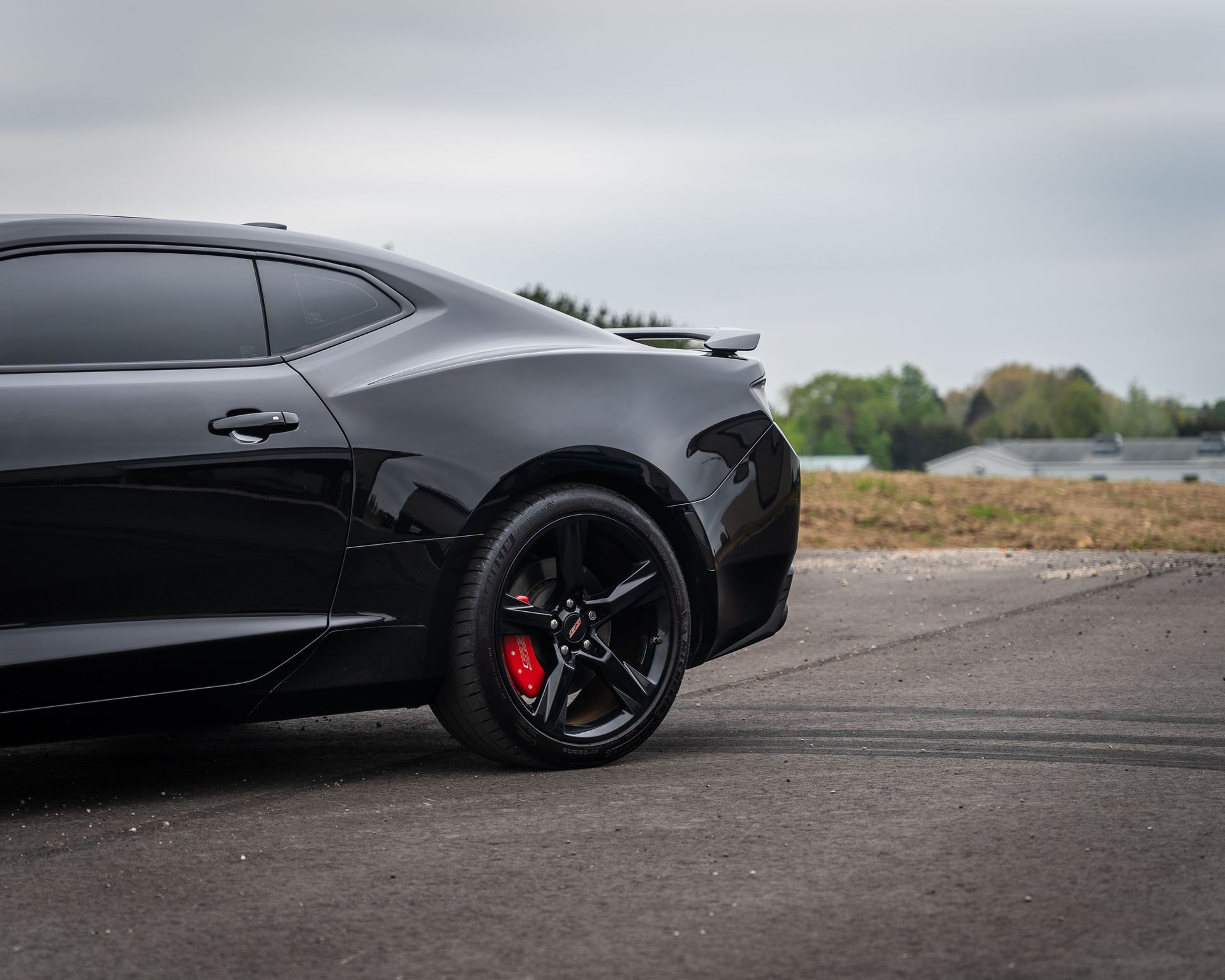 Side profile of a black Chevrolet Camaro with tinted windows and red brake calipers parked on an asphalt road.