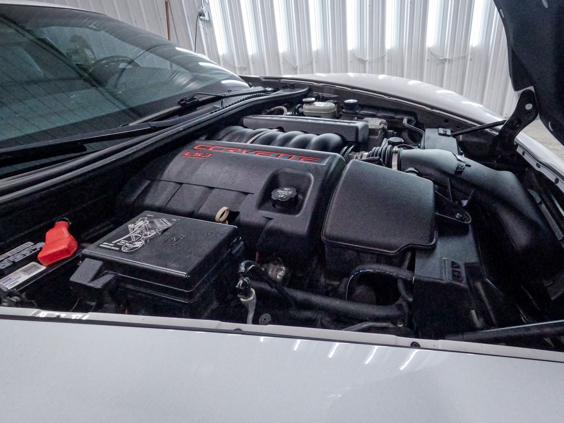 The engine bay of a silver BMW featuring a black engine cover and an aftermarket carbon fiber cold air intake.