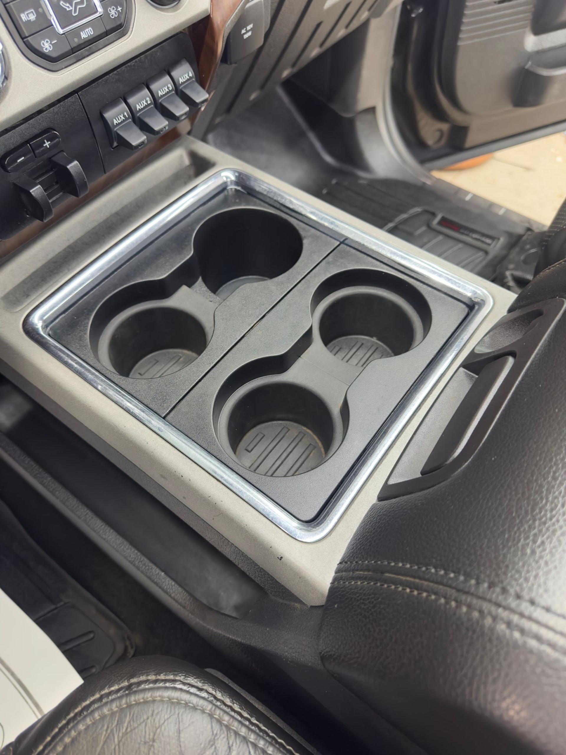 A view of a vehicle's center console featuring a four-slot black plastic cupholder with a silver metal trim border.